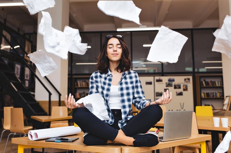 woman meditating on table surround work stuff and flying papers